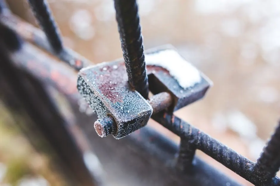 Close-up of a frosty, rusted padlock on an iron fence during winter season.